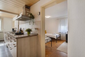 A modern kitchen with a central island, a bed with a white duvet, and a window with sheer curtains.