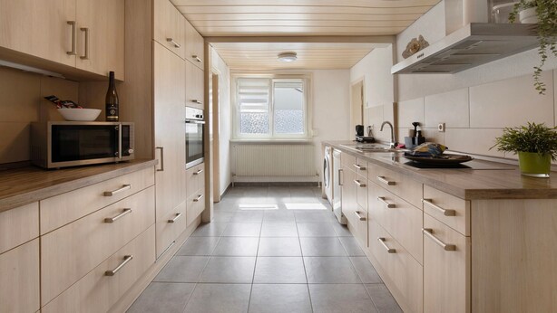 A modern kitchen with wooden cabinets, a microwave, a wine bottle, and a window. - M B Homes Nürtingen with Wi-Fi (Nürtingen)