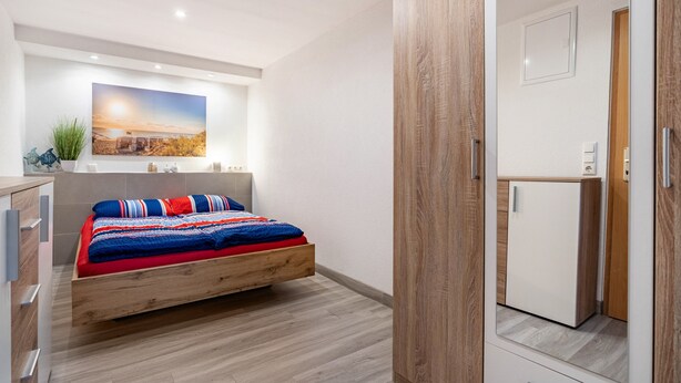 A bedroom with a bed, a small white cabinet, and a large mirror.