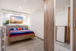 Une chambre à coucher avec un lit, une petite armoire blanche et un grand miroir.