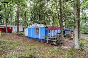 Une petite cabane bleue, surmontée d’un parasol rouge, entourée d’arbres.