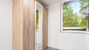 A room with a wooden wardrobe, a window with a view of trees, and a white wall.