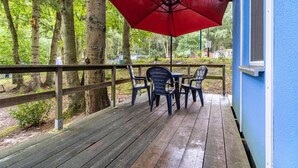 A wooden deck with a red umbrella, two chairs, and a table.