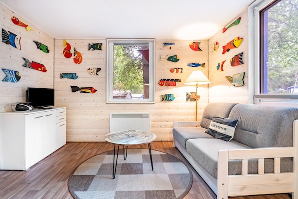 Une pièce avec un mur en bois, un canapé, une télévision, une table et une fenêtre.