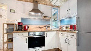 Une cuisine moderne équipée d’une cuisinière, d’un four et d’un réfrigérateur, avec des meubles en bois et une vue sur la plage par la fenêtre.