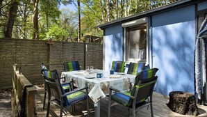 Une terrasse en bois avec une table dressée pour six personnes, entourée de chaises dotées de coussins à rayures.