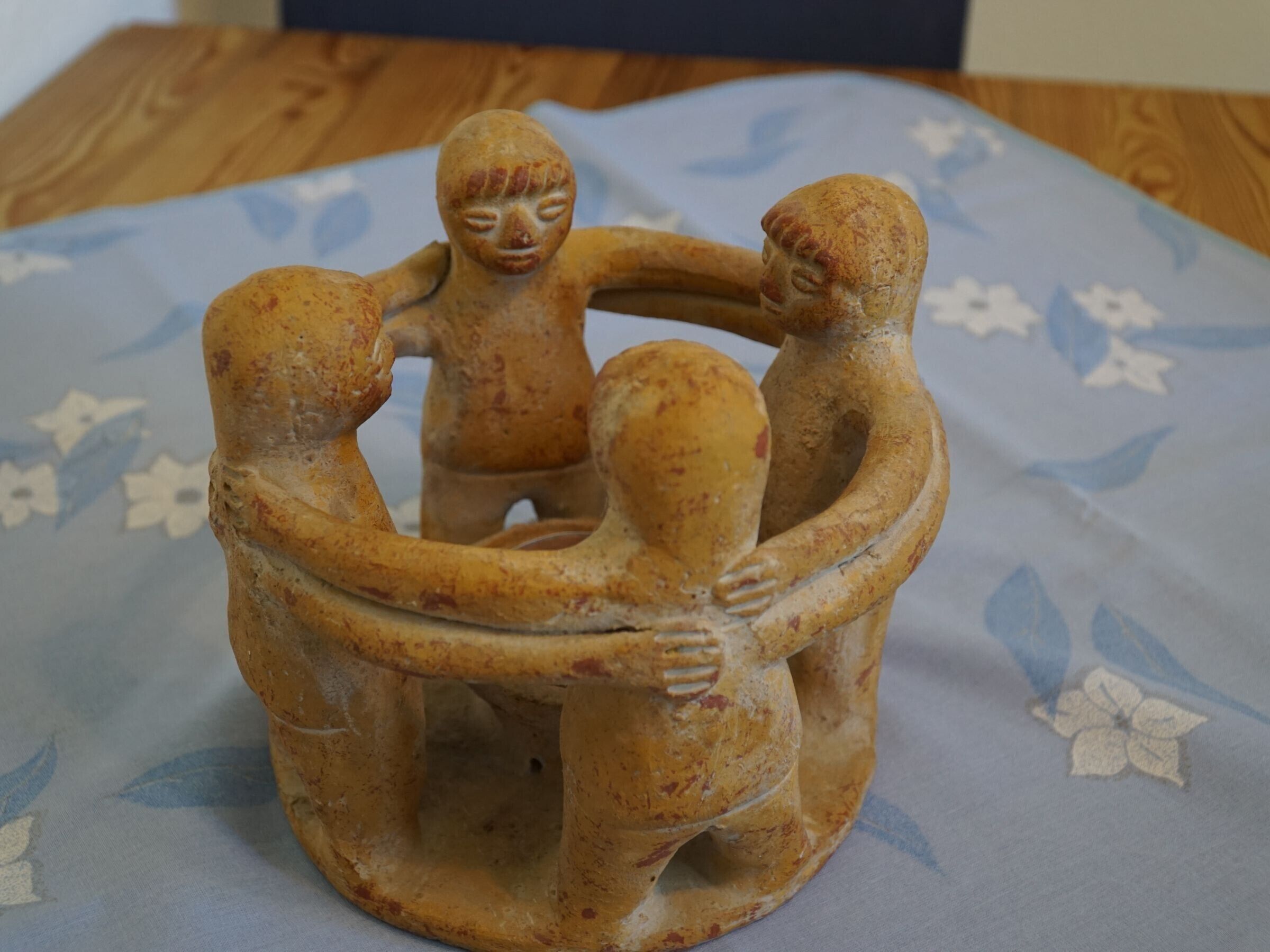 A wooden sculpture of three figures in a circle on a table.