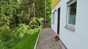 A pathway leading to a building with a window and a door, surrounded by greenery and trees. - Apartment 'Am Eschachwäldle' with Private Terrace, Private Garden and Wi-Fi (Niedereschach)