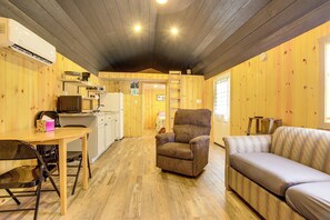 L’intérieur chaleureux d’un chalet avec un plancher en bois, une table à manger avec des chaises, un canapé, un fauteuil et un coin cuisine.
