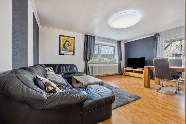 Una sala de estar moderna con un sofá de cuero, una mesa de centro de madera, un televisor y un escritorio con una silla.