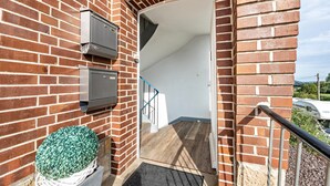 A brick exterior with a door leading to a staircase, a small white basket with a plant, and a metal railing.