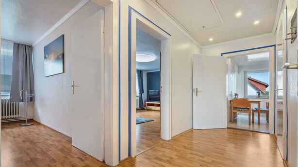 A modern interior with wooden flooring, white walls, and a dining area with a table and chairs.