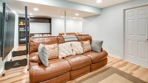 Ein Wohnzimmer mit einem braunen Ledersofa, einem Laufband und einem Bücherregal mit Kinderspielzeug.