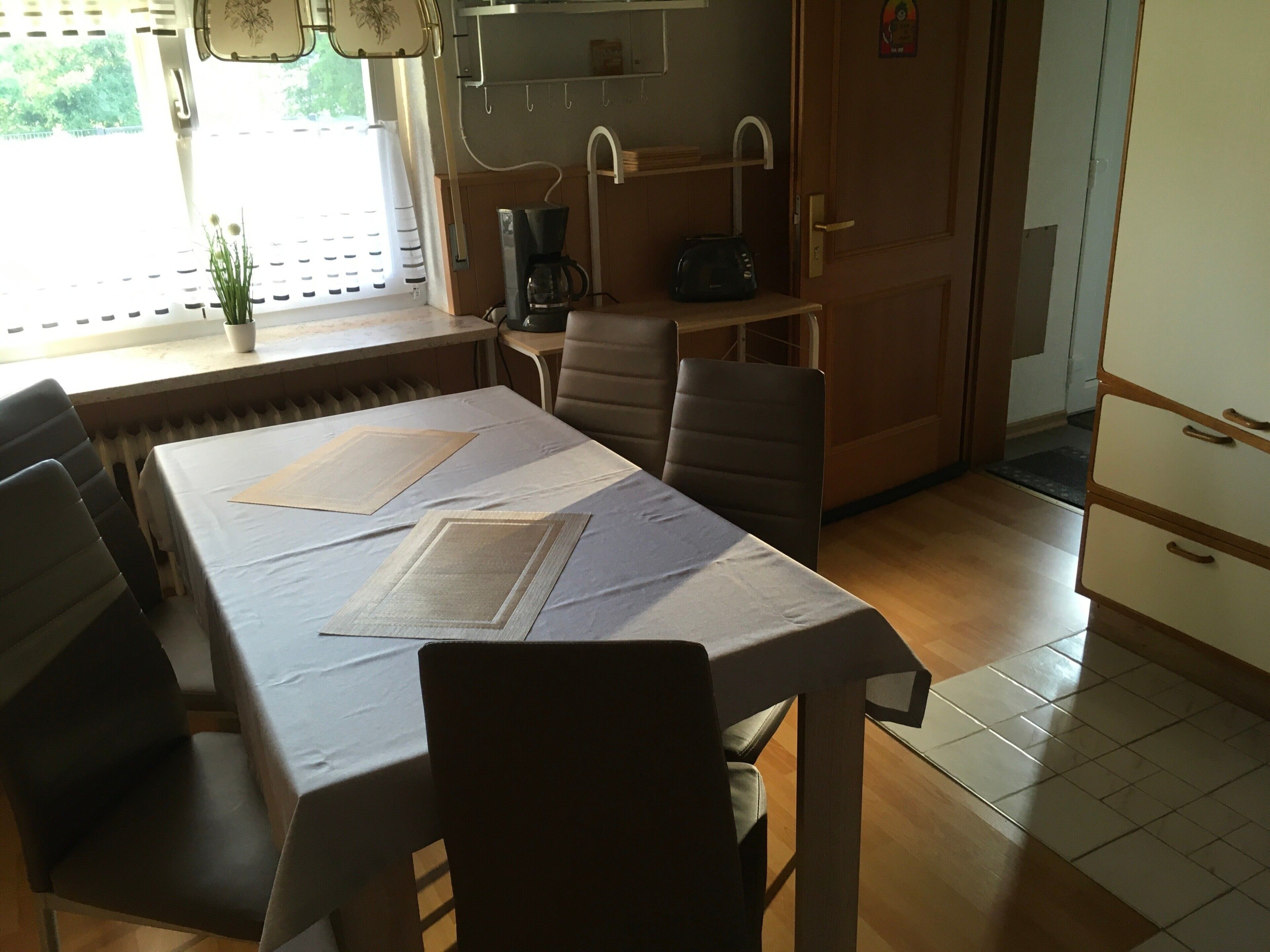 A dining area with a table set for two, chairs, a radiator, a coffee maker, and a toaster.