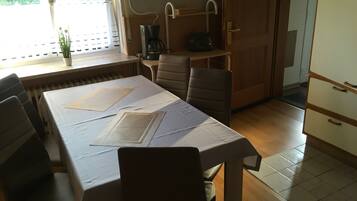 A dining area with a table set for two, chairs, a radiator, a coffee maker, and a toaster.