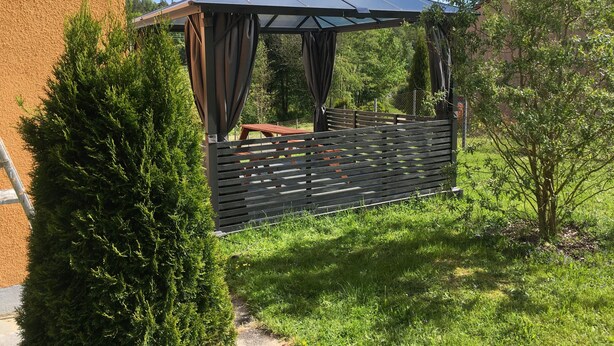 A gazebo with a roof and curtains, surrounded by greenery and a wooden fence. - Apartment 'Fewo Eberau' with Shared Garden and Wi-Fi (Ebrach)