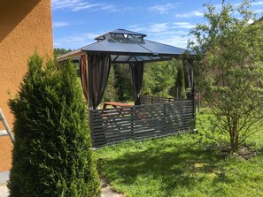 A gazebo with a roof and curtains, surrounded by greenery and a wooden fence. - Apartment 'Fewo Eberau' with Shared Garden and Wi-Fi (Ebrach)