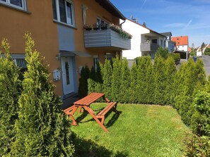 Un immeuble résidentiel doté d’un balcon, d’une porte et d’une petite pelouse avec un banc en bois.