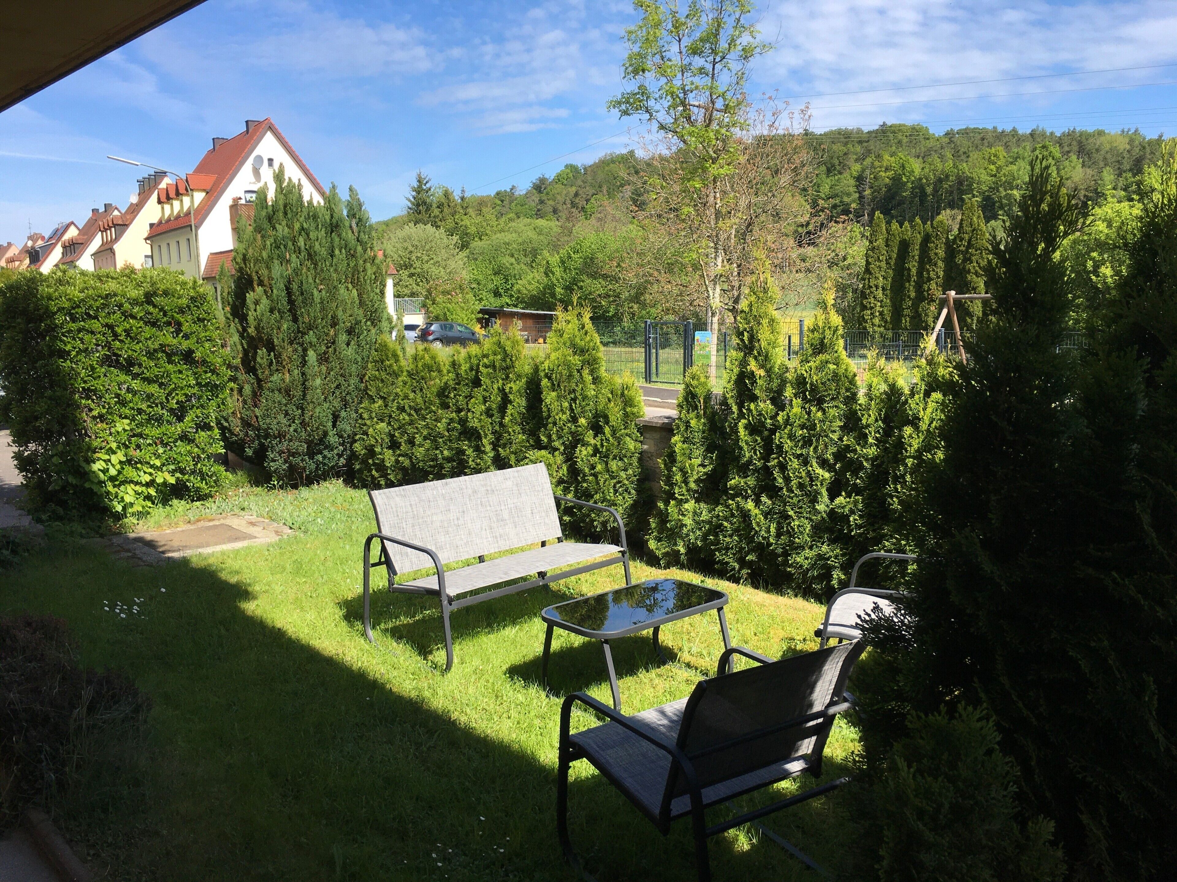 Un patio con panchina e tavolo, immerso nel verde e affacciato su case e alberi.