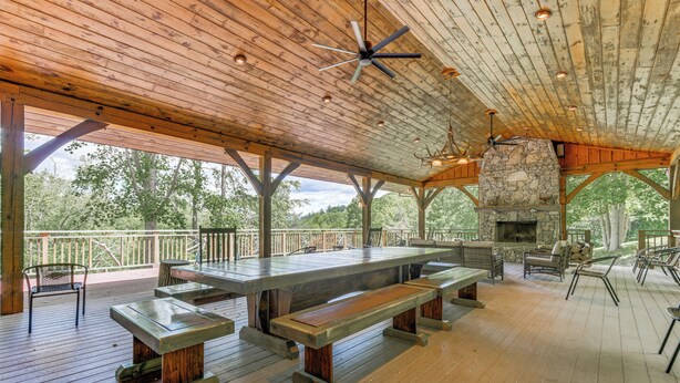 Une terrasse extérieure couverte, dotée d’une cheminée en pierre, de bancs en bois et d’une longue table à manger.