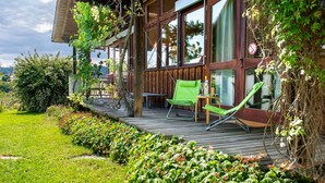 Une terrasse en bois avec une table et des chaises, entourée d’une végétation luxuriante et offrant une vue sur la campagne.