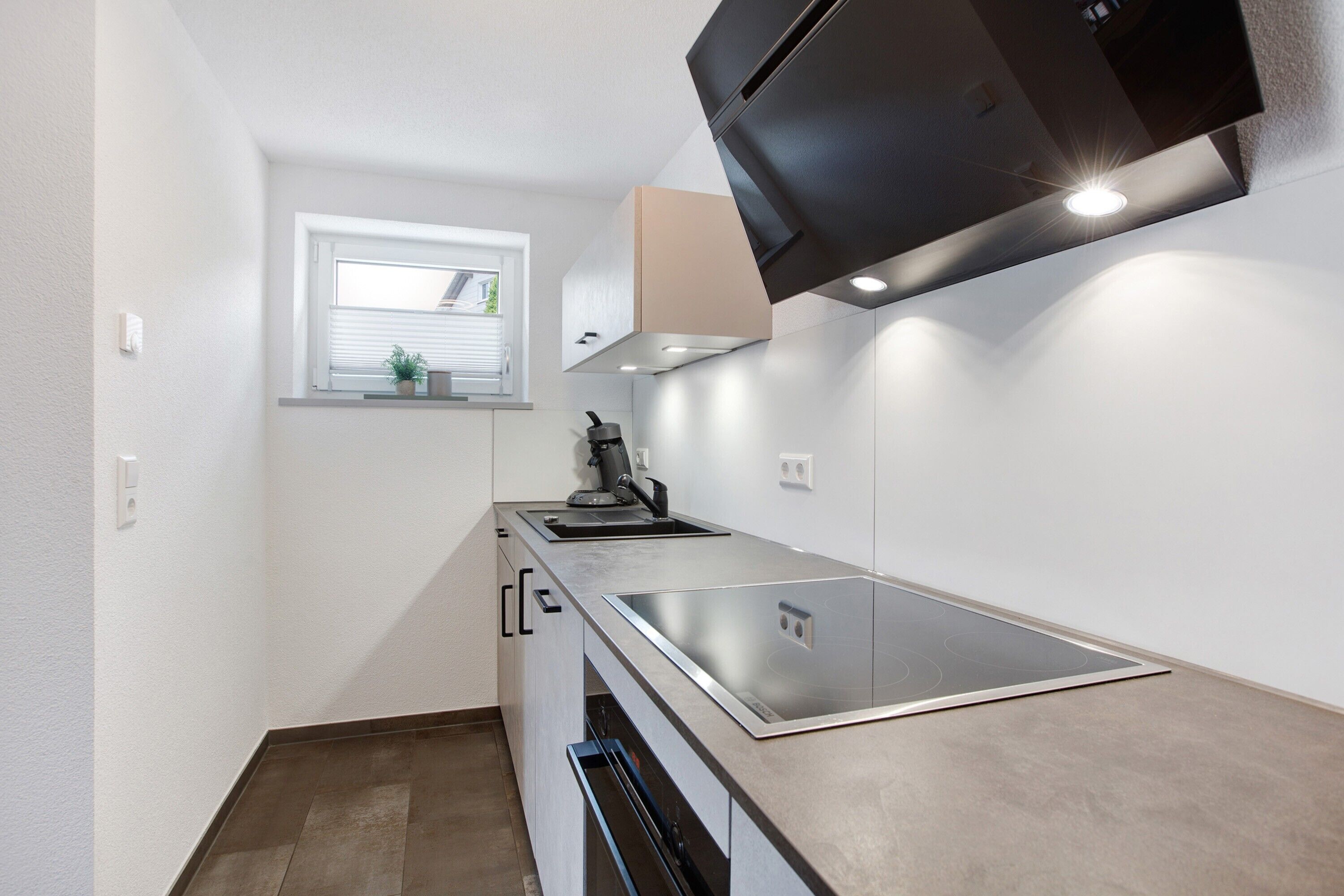 A compact kitchen with a built-in stove, a window, and a black range hood.