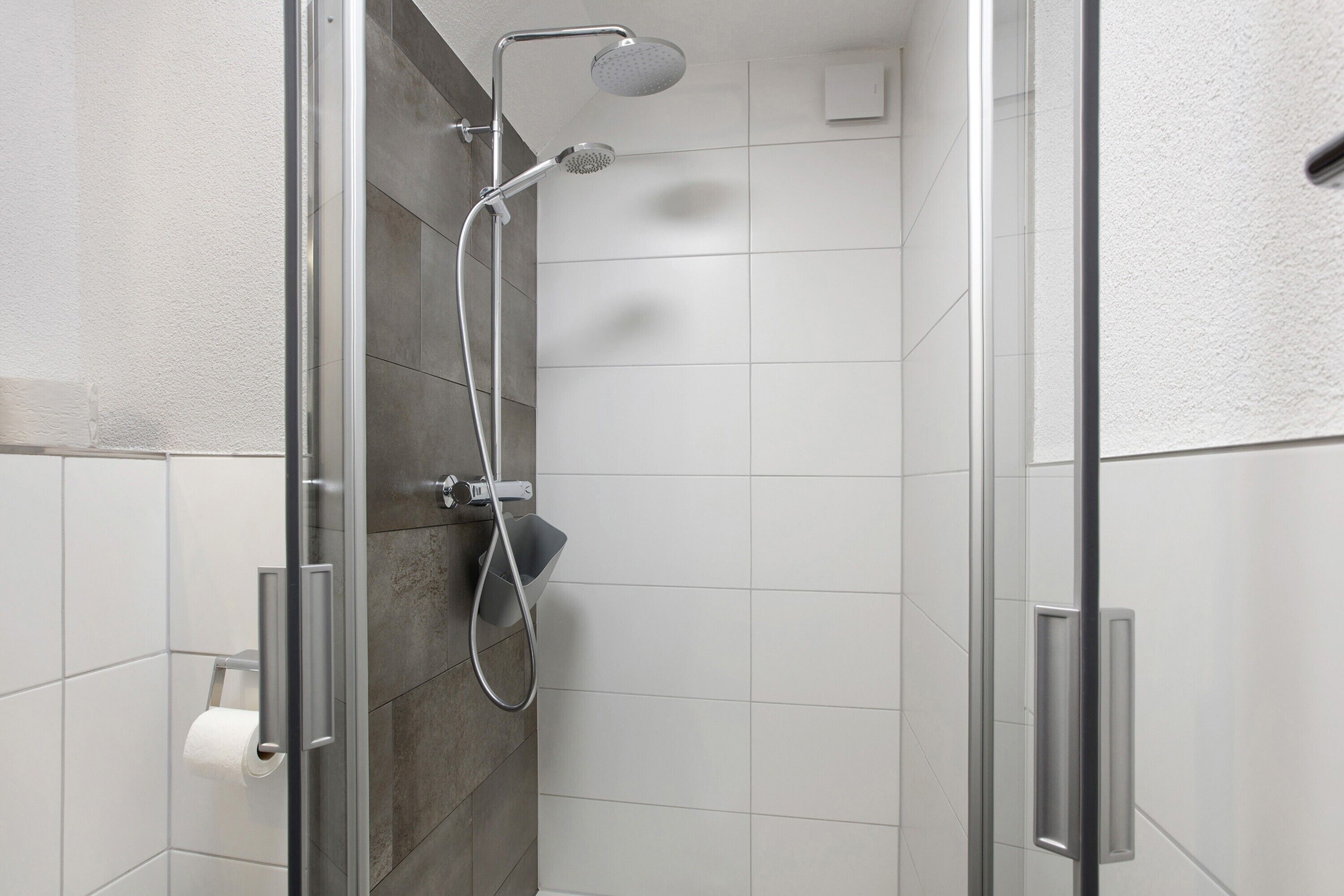 Um chuveiro moderno com porta de vidro, um chuveiro manual e uma torneira fixada na parede.