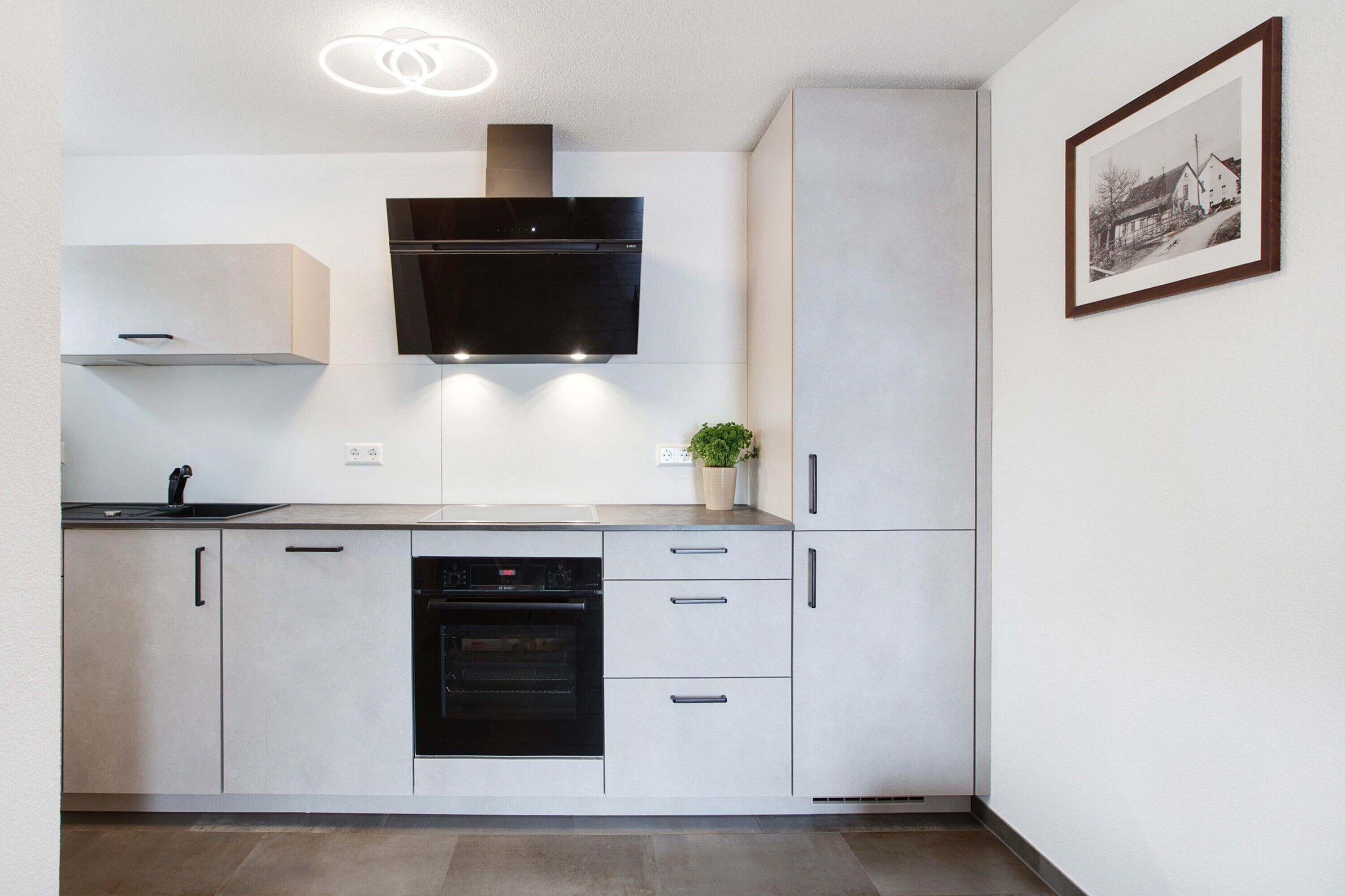 A modern kitchen with a built-in oven, a black range hood, and a small potted plant.