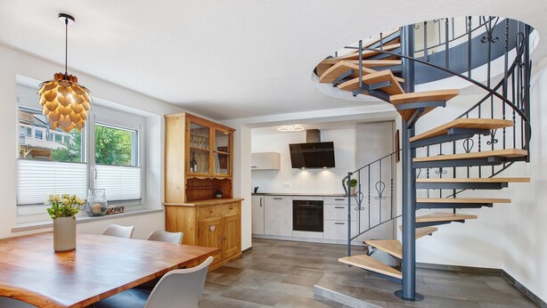Une cuisine moderne avec un escalier en colimaçon, des meubles en bois et un coin repas comprenant une table et des chaises.