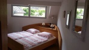 Une chambre à coucher avec un lit en bois, deux fenêtres, une table de chevet, une lampe et un miroir.