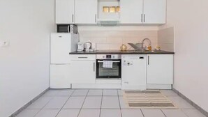 Una cocina compacta con armarios blancos, microondas, horno y lavavajillas.