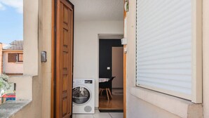Un estrecho pasillo que da a una habitación con lavadora, una puerta y un ventanal con persianas.