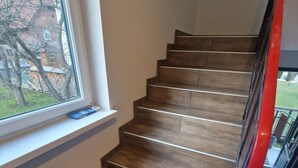 Eine Holztreppe mit roter Handlauf, ein Fenster mit Blick auf einen Garten und ein blaues Objekt an der Fensterbank.