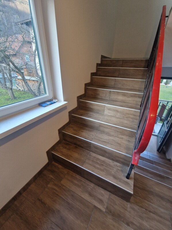 A wooden staircase with a red handrail, a window with a view of a garden, and a blue object on the windowsill.
