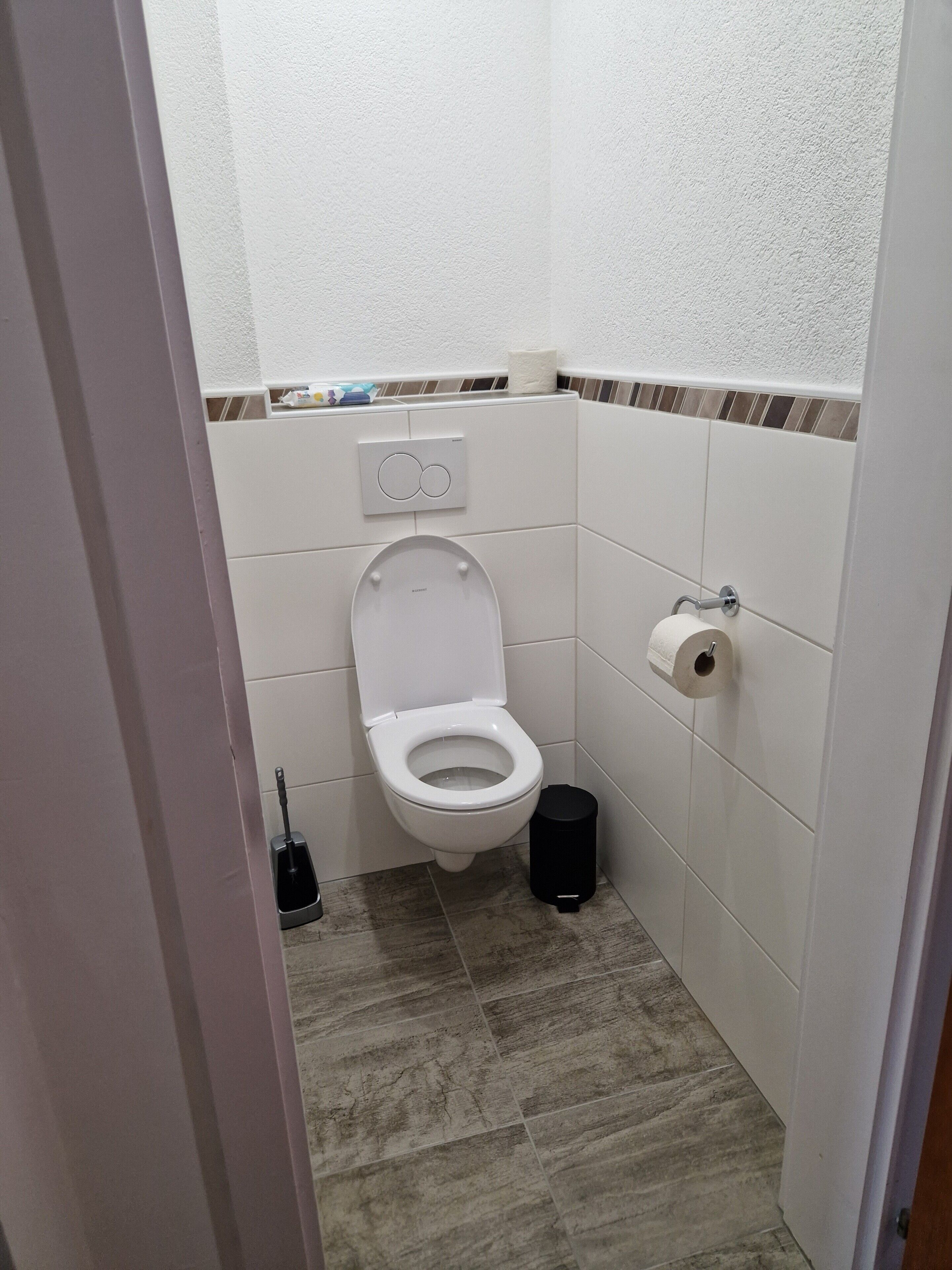 A small, clean bathroom with a toilet, a trash bin, and a toilet paper holder.