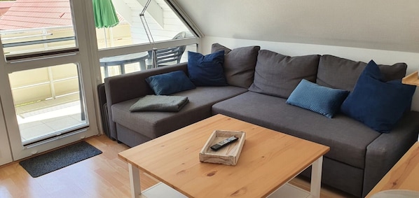 Un salon moderne avec un canapé, une table basse en bois et une porte en verre donnant sur un espace extérieur.