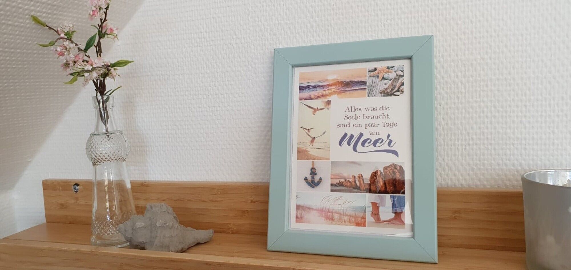 A framed collage with text and images, a vase with flowers, and a candle on a wooden shelf.