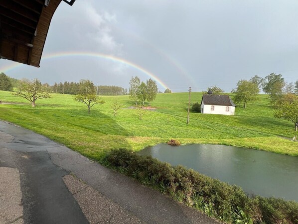 A rural landscape with a house, a pond, and a rainbow.