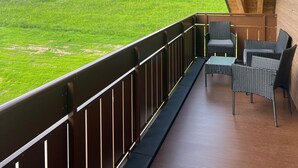 A balcony with a view of a green field, wooden beams, and wicker furniture. - Holiday Home Ferienhaus am Kapellenhof with Shared Terrace, Shared Garden and Wi-Fi (Triberg im Schwarzwald)