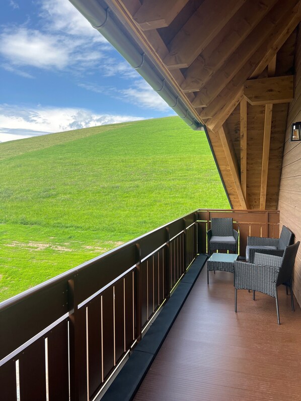 A balcony with a view of a green field, wooden beams, and wicker furniture.