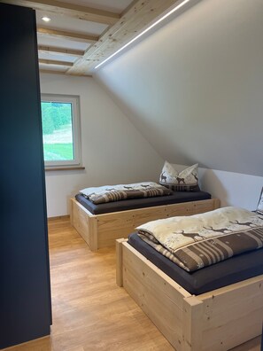 Une chambre avec deux lits en bois, une fenêtre et un plafond en pente.