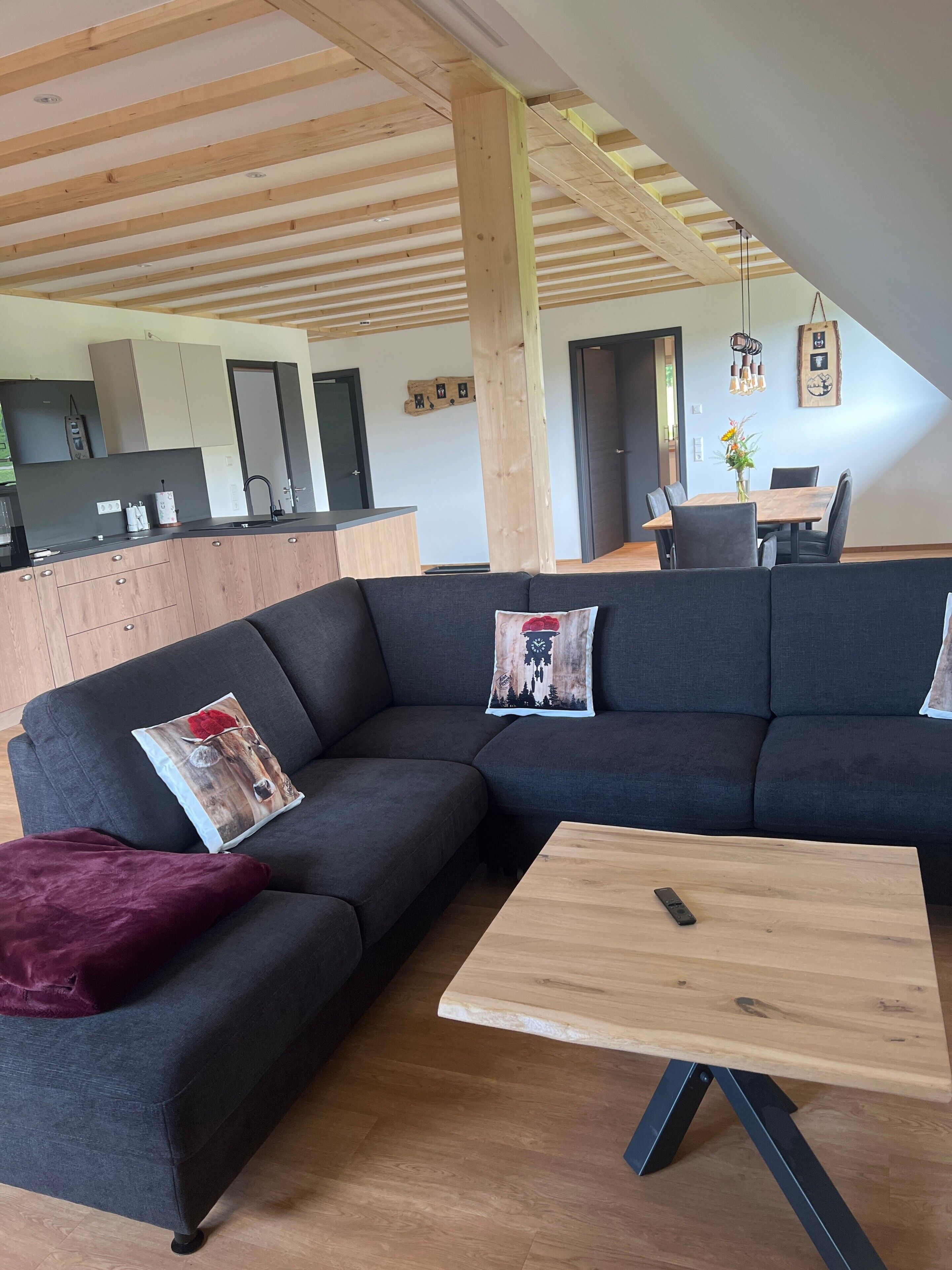 Una sala de estar moderna con un sofá modular, una mesa de centro de madera y una cocina al fondo.