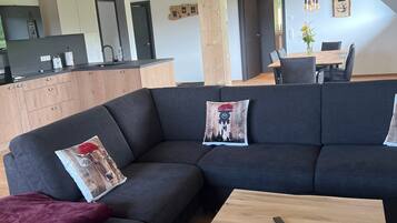 Una sala de estar moderna con un sofá modular, una mesa de centro de madera y una cocina al fondo.