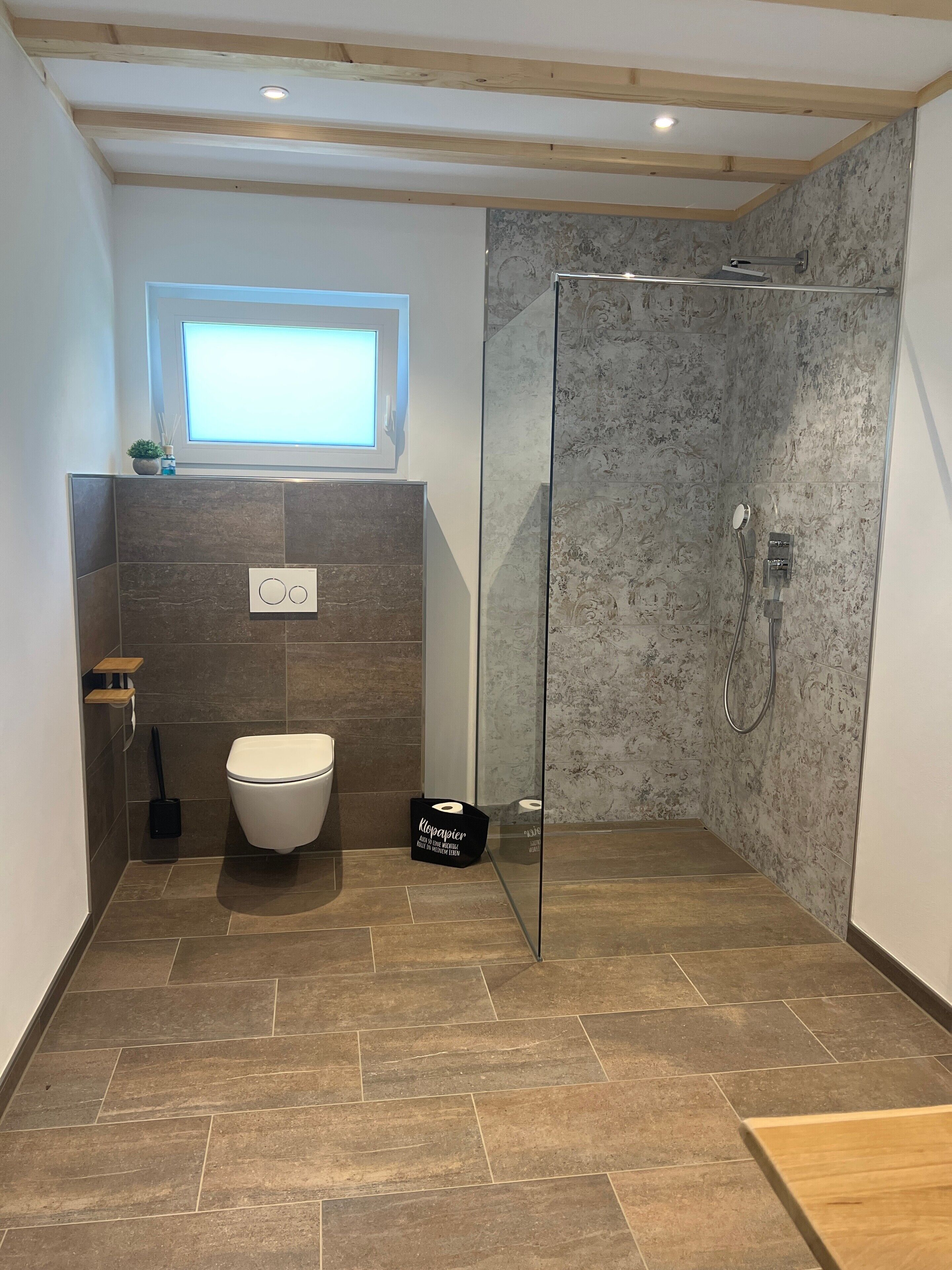 Een moderne badkamer met toilet, douche en een klein raam.