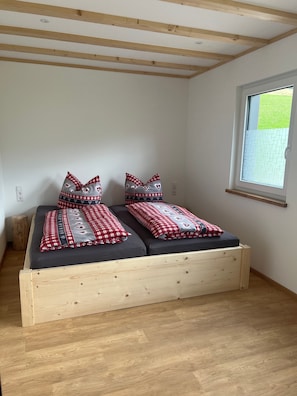 Quarto com cama de madeira, janela com vista e um banquinho pequeno.