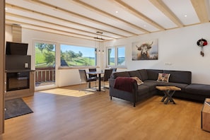 Een moderne woonkamer met een houten plafond, een grijze bank, een eettafel en een keuken met een oven.