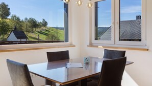 A dining area with a table and chairs, large windows with a view of a green landscape. - Apartment 'Kapellen Blick' with Mountain View, Shared Terrace and Wi-Fi (Triberg im Schwarzwald)