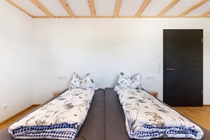 A room with two single beds, a dark door, and a wooden ceiling.