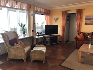 Uma sala de estar com televisão, móveis de vime e um quadro na parede.