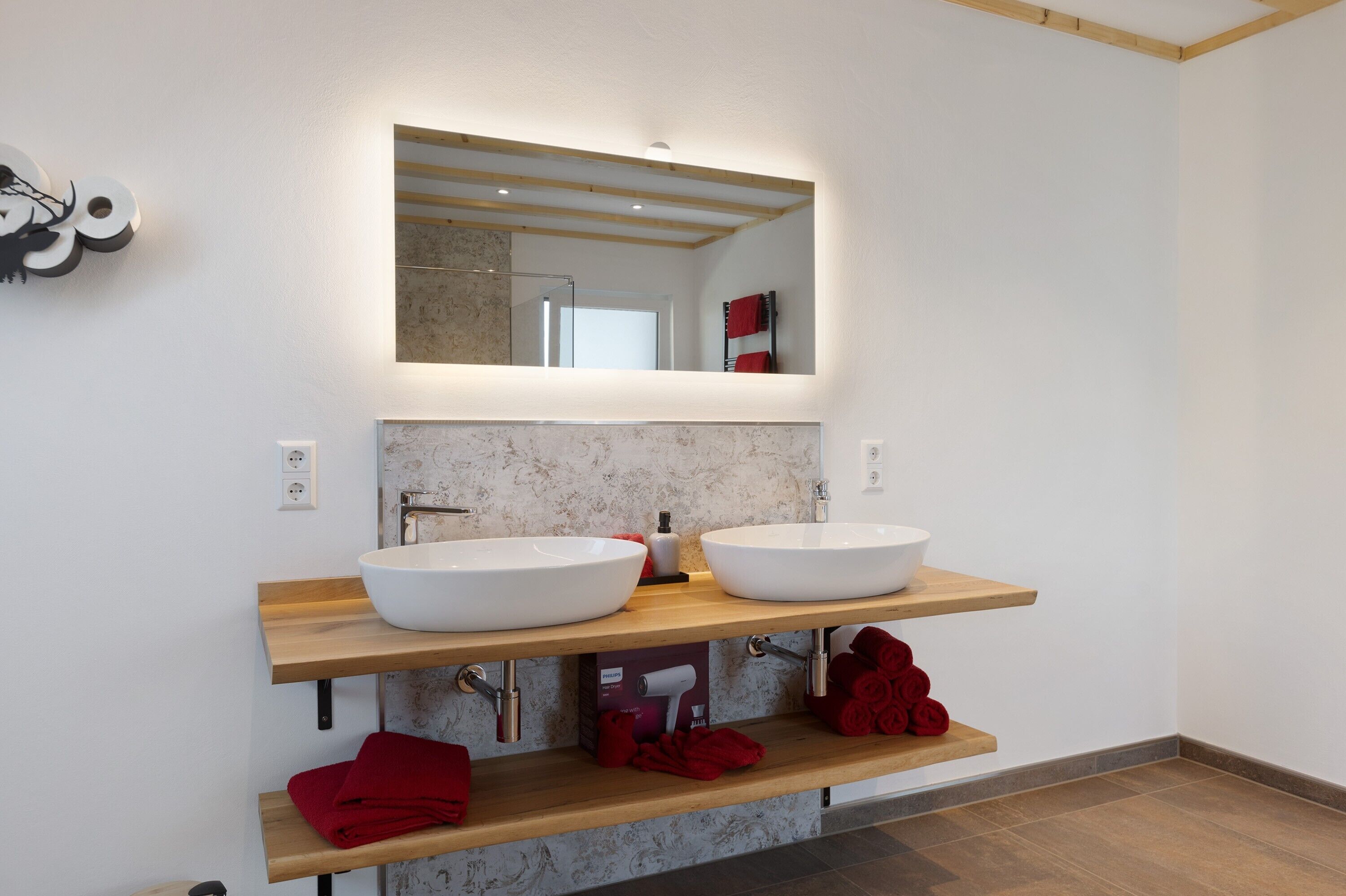 A modern bathroom with two white sinks, a large mirror, and wooden shelves.